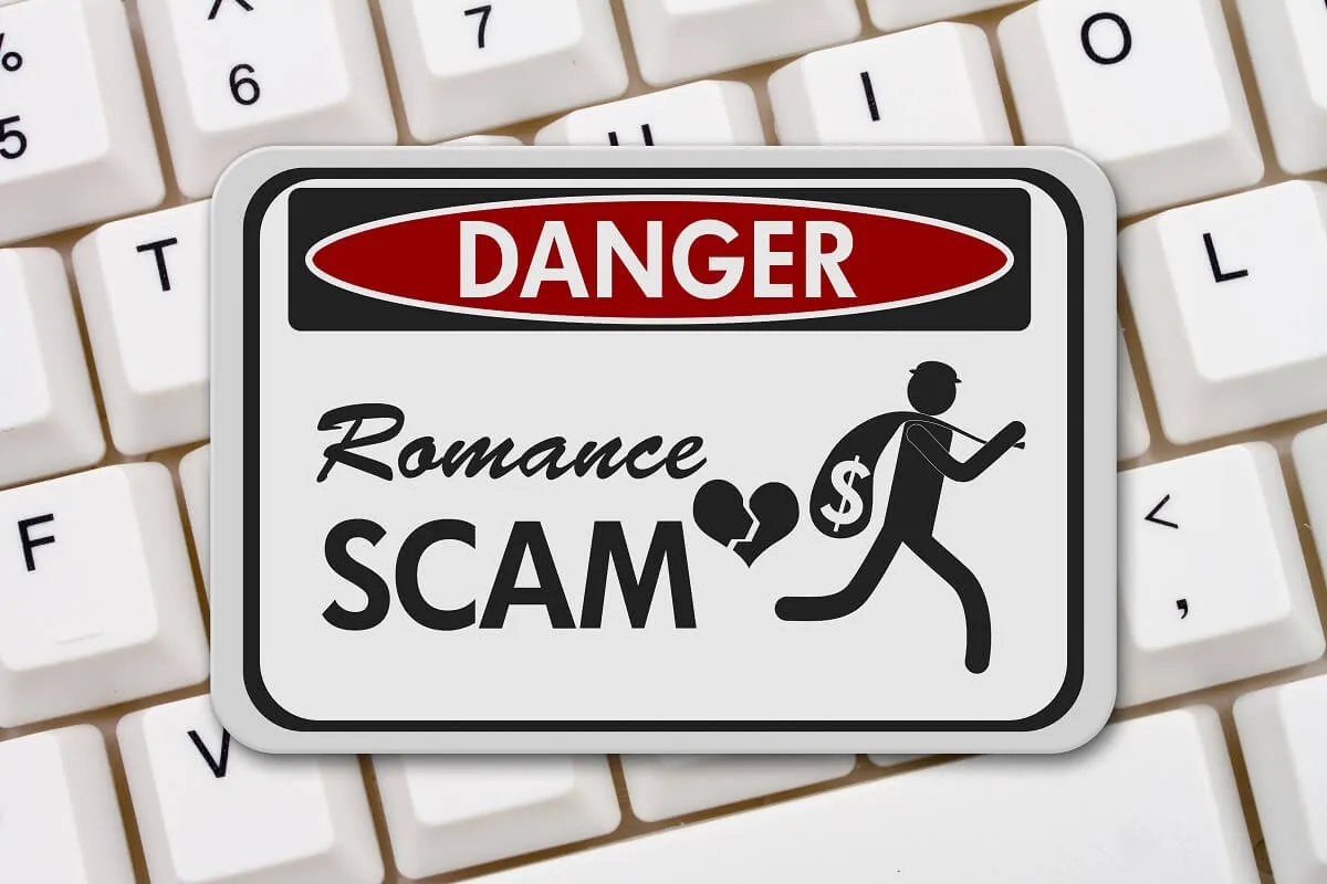 Warning sign highlighting the danger of romance scams over a keyboard background.