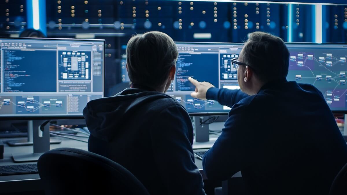 Two cybersecurity professionals analyzing data on multiple monitors in a dark office.